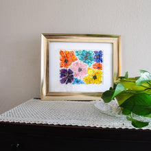Load image into Gallery viewer, Framed artwork of colorful flowers on a white background, placed on a textured surface with a plant in the corner.