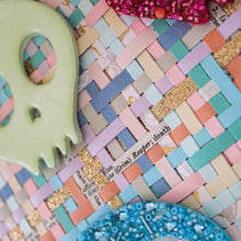 Load image into Gallery viewer, Decorative skulls on a colorful woven surface with text