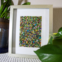 Load image into Gallery viewer, Framed abstract artwork with multicolored dots on a textured surface with plants.
