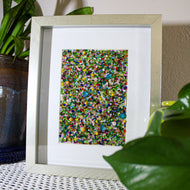 Framed abstract artwork with multicolored dots on a textured surface with plants.