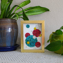 Load image into Gallery viewer, Framed artwork with colorful abstract design on a table with plants in the background
