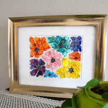 Load image into Gallery viewer, Framed artwork with colorful floral design on a textured surface with a plant.
