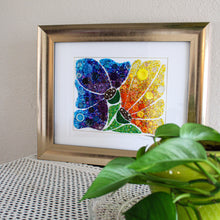 Load image into Gallery viewer, Framed colorful abstract artwork on a textured surface with a plant in the foreground.
