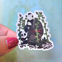 Load image into Gallery viewer, Sticker of two pandas holding bamboo leaves with a blurred light blue background
