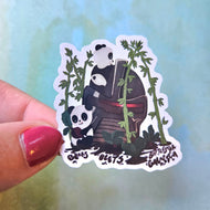 Sticker of two pandas holding bamboo leaves with a blurred light blue background