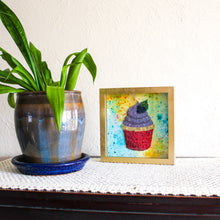 Load image into Gallery viewer, Framed artwork of a colorful cupcake next to a potted plant on a wooden surface.
