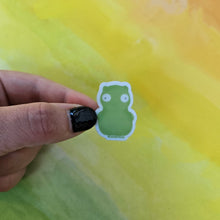 Load image into Gallery viewer, Hand holding a small green sticker against a yellow and green abstract background
