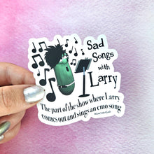Load image into Gallery viewer, Sticker with 'Sad Songs with Larry' design held by a hand against a pink and purple gradient background.

