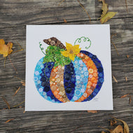 Colorful mosaic pumpkin art on a wooden surface with autumn leaves.