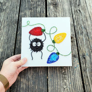 Handmade embroidered card with a soot sprite and colorful lights on a wooden surface