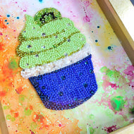 A handcrafted bead art in the shape of a cupcake with green and white colors, decorated with blue and clear beads and Swarovski crystals.