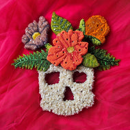 Hand-beaded floral skull artwork with a wired and felted back, adorned with glass beads and Swarovski crystals, against a pink background.